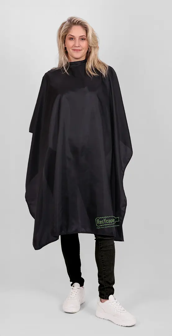 TrendDesign – Modeumhang Frau in einem schwarzen Umhang von TrendDesign, steht vor einer weißen Wand.